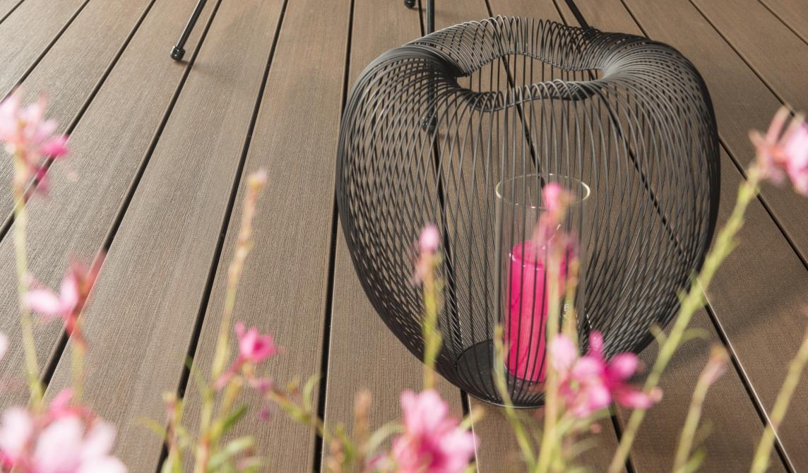 Photo studio d'une terrasse avec des fleurs en premier plan et un objet de décoration posée sur la terrasse