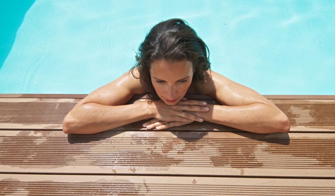 Femme les bras posés sur une plage de piscine en bois composite de couleur brun exotique